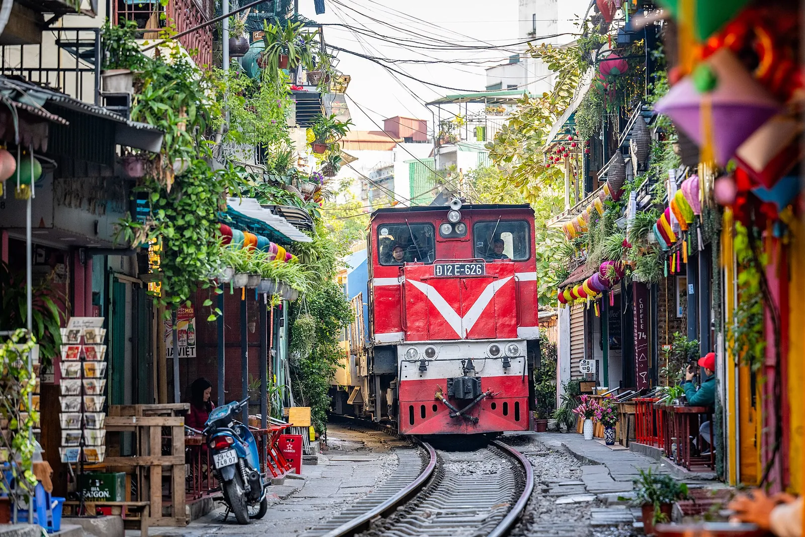 A train passing through Hanoi's train street, between houses, cafés and potted plants