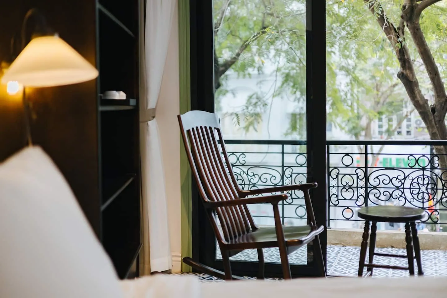 A rocking chair on the balcony of Thu, with the trees of Ba Trieu Street outside